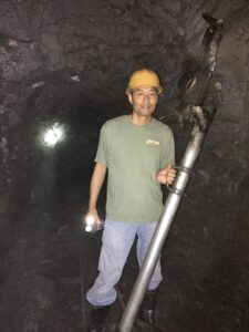 Zhouping “Charlie” Guo shown inside a Chinese mine wearing a hard hat and holding mining equipment
