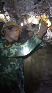 Zhouping “Charlie” Guo shown inside a Chinese mine, wearing a hardhat, taking photographs of minerals in situ.