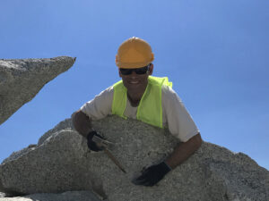 Dr. John Jaszczak in mining gear, posing over a large boulder