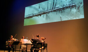 The image Cylindrical_Whiskers-3crop is of a string quartet playing a composition "Cylindrical Whiskers (merelaniite)" by Libby Meyer that was inspired by the new (criminal) mineral merelaniite (image of one on the screen) and played in the Rosza Performing Arts Center for its world premier on 10/17/2019