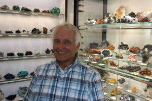 Les in his studio with display cases filled with minerals behind him